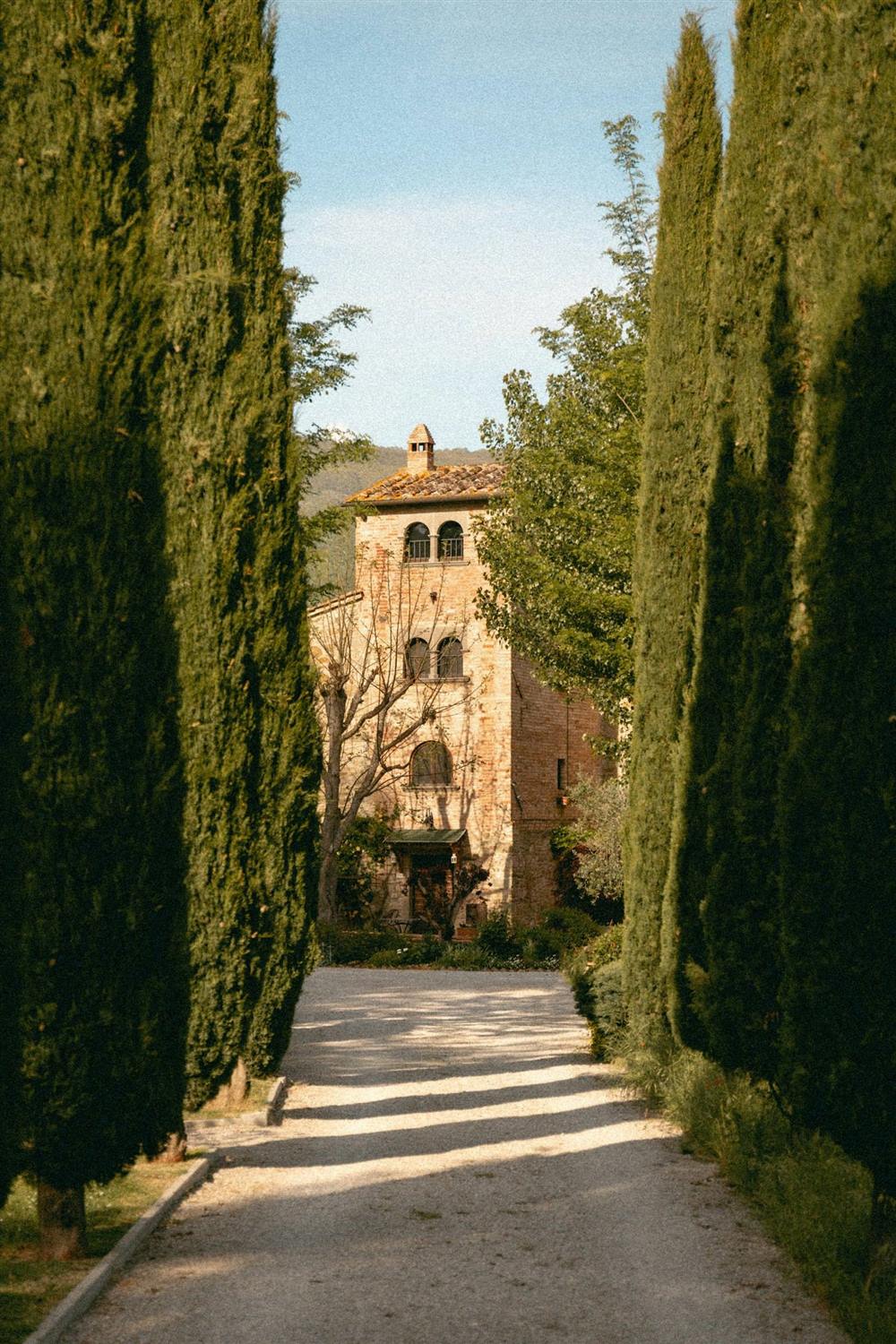 Viale di cipressi che conduce a un casale in pietra toscano